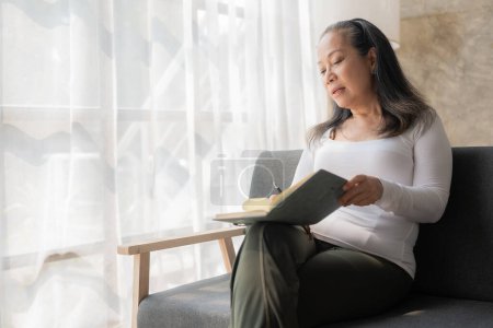 Photo for Asian senior woman reading a book on the sofa at home Activity ideas for the elderly in the family. - Royalty Free Image