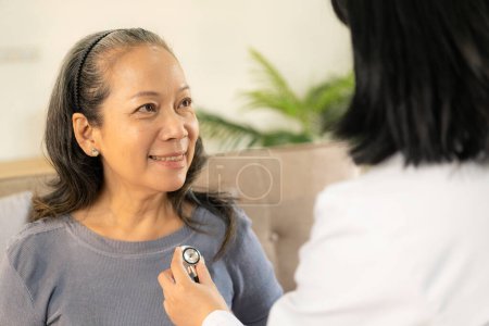 Foto de Médico examinando el corazón con estetoscopio y hablando con la mujer mayor en la clínica para el chequeo anual y el concepto de seguro de salud. - Imagen libre de derechos