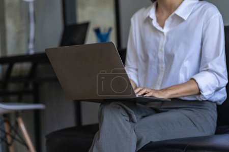Foto de Vista lateral de las manos de la mujer de negocios utilizando la computadora portátil en reposo, mujer joven escribiendo en un cuaderno en blanco colocado en la mesa de la oficina con el teclado del ordenador portátil fotos de cerca - Imagen libre de derechos