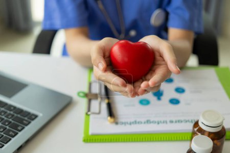 Foto de Médico femenino sosteniendo bola roja en forma de corazón explicando al paciente en línea en el ordenador portátil Concepto de cardiología, servicios de salud, médico - Imagen libre de derechos
