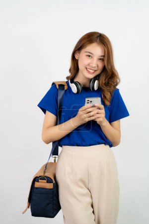 Photo for Asian girl using smartphone in blue shirt and backpack on background while standing and mobile phone isolated on white background - Royalty Free Image