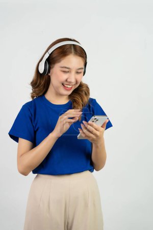 Foto de Bastante feliz asiática adolescente utilizando el teléfono móvil reproducción de música desde la aplicación de teléfono inteligente, feliz sonriendo mientras escucha streaming de música sobre fondo blanco, concepto de tecnología - Imagen libre de derechos