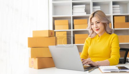 Téléchargez les photos : Belle jeune femme asiatique travaillant avec boîte de vente en ligne avec ordinateur portable prenant des commandes en ligne à la maison, concept d'entreprise PME - en image libre de droit