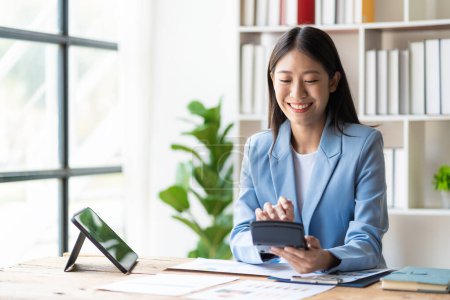 Photo for Happy young Asian business woman working with financial documents and laptop and smartphone - Royalty Free Image