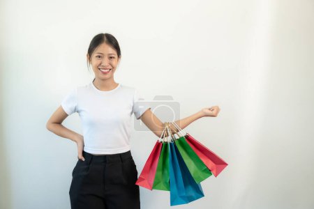 Téléchargez les photos : Jeune femme asiatique souriant et levant les bras tenant des sacs à provisions, isolée sur fond blanc, concept de shopper - en image libre de droit
