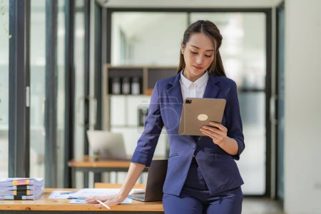 Foto de Mujer de negocios asiática sosteniendo tableta digital y de pie delante de su escritorio, concepto creativo Mujer de negocios exitosa en los negocios - Imagen libre de derechos