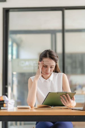 Photo for Contemplative Asian female executive in shirt working with laptop in modern office Take notes and come up with a professional plan. Project management Consider financial business concepts. - Royalty Free Image