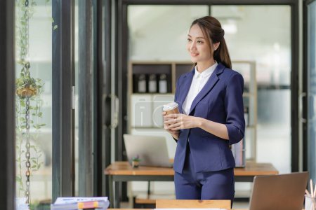 Téléchargez les photos : Femme d'affaires asiatique travaillant avec des papiers et un ordinateur portable assis à la table au bureau, analysant les calculs de comptabilité d'entreprise et les concepts de planification financière. - en image libre de droit