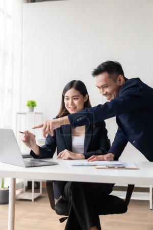 Téléchargez les photos : Deux hommes et femmes d'affaires asiatiques souriant heureux de travailler avec des ordinateurs portables et des documents financiers. Ils parlent de leurs projets et réfléchissent ensemble à des idées créatives au bureau.. - en image libre de droit