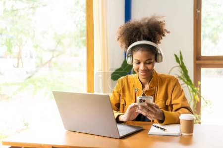 Téléchargez les photos : Jeune femme africaine étudiant en ligne avec ordinateur portable dans un café Millennial African American girl avec casque travaillant sur ordinateur portable dans un café - en image libre de droit