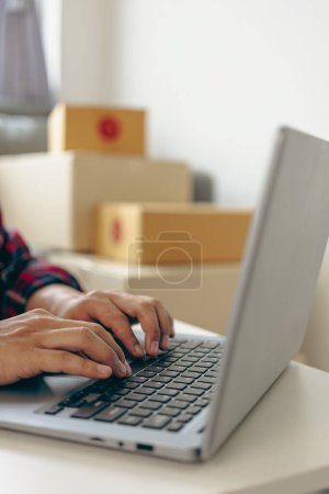 Téléchargez les photos : Gros plan d'un jeune homme vendant en ligne avec une boîte jaune, travaillant en ligne avec un ordinateur portable prenant des commandes de clients. Concept d'entreprise PME. Image verticale. - en image libre de droit
