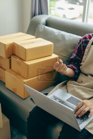 Photo for Closeup of a young man selling online with a yellow box, working online with a laptop taking orders from customers. SME business concept. Vertical image. - Royalty Free Image