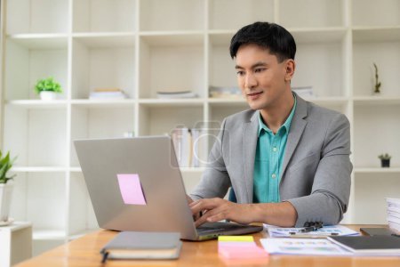 Téléchargez les photos : Homme d'affaires asiatique travaillant au bureau avec ordinateur portable et documents sur la table Travail sur le lieu de travail, documents d'affaires, concepts de planification financière - en image libre de droit