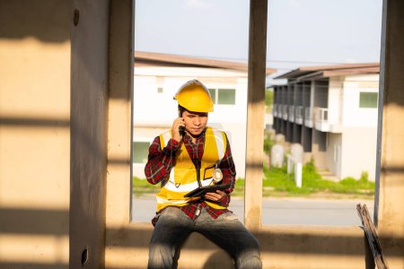 Foto de Joven ingeniero asiático inspecciona la arquitectura, concepto de proyecto de construcción, joven ingeniero profesional en casco y papel plano en el sitio de construcción de la casa. - Imagen libre de derechos