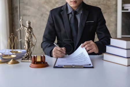 Photo for Asian male lawyer working in a law office with a judge's gavel and a weight scale on the table, legal consulting concept. - Royalty Free Image