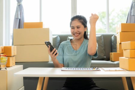 Foto de Mujer asiática Revisar pedidos de clientes en computadoras portátiles y teléfonos móviles. Negocios en línea y concepto de envío - Imagen libre de derechos