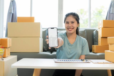 Téléchargez les photos : Asiatique femme Revoir les commandes de clients sur les ordinateurs portables et les téléphones mobiles. Concept d'affaires et d'expédition en ligne - en image libre de droit