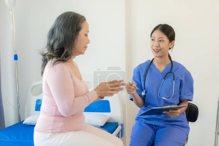 Téléchargez les photos : Femme asiatique médecin parle au patient avec le sourire pour encourager le patient à l'hôpital Une femme asiatique âgée rend visite à un médecin dans un bureau de l'hôpital. Parlez des résultats de l'examen de santé - en image libre de droit