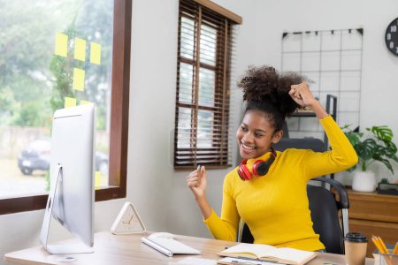 Téléchargez les photos : Fille afro-américaine excitée portant des écouteurs étudiant en ligne sur ordinateur portable Happy mixte femme célèbre le succès tout en travaillant à distance de la maison. - en image libre de droit
