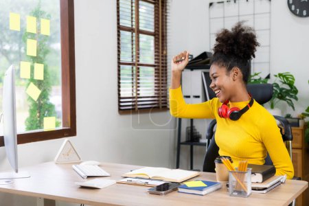 Photo for Excited African American girl wearing headphones studying online on laptop Happy mixed race woman celebrates success while working remotely from home. - Royalty Free Image