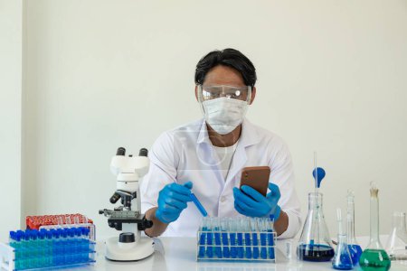 Photo for Scientist picks up sample tube of blue badger chemical along with analyzer in lab Technician holding test tubes in lab for research - Royalty Free Image