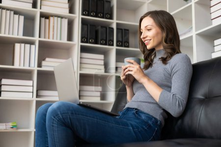 Photo for Beautiful young woman sitting on sofa looking at laptop screen Millennial students who are motivated to study remotely from home I am a female freelancer who works online. - Royalty Free Image