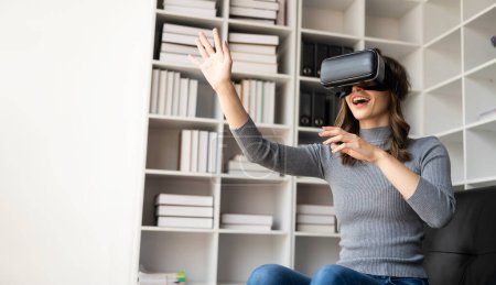 Photo for Happy young woman surprised in VR headset, feeling air. Smiling caucasian woman wearing vr glasses, virtual reality technology device, watching 3d simulation video while sitting on sofa at home. - Royalty Free Image