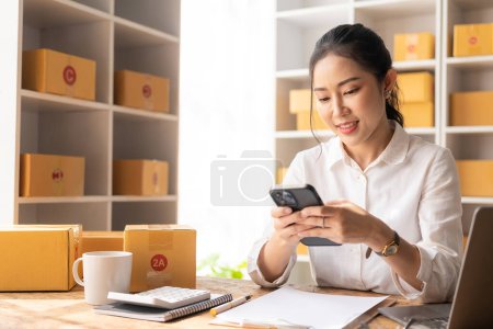 Photo for Asian woman talking on smartphone with customer, keying commands with laptop, small business, e-commerce and online shopping, small and new business entrepreneur, retail business, SME - Royalty Free Image