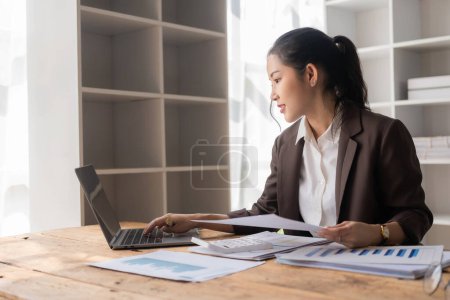 Téléchargez les photos : Belle femme d'affaires asiatique analyse des graphiques à l'aide d'une calculatrice sur ordinateur portable au bureau avec des documents sur la table Planification d'analyser les rapports financiers plan d'affaires investissement - en image libre de droit