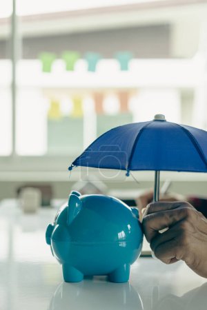 Téléchargez les photos : Lignes directrices sur l'assurance des biens avec un parapluie sur une tirelire et une pile de pièces sur une table - en image libre de droit