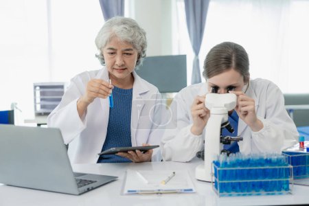 Foto de Hermosa científica joven y dos mujeres mayores trabajan en un laboratorio con tubos de ensayo que investigan los productos químicos azules en la industria de la salud. - Imagen libre de derechos