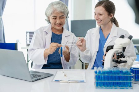 Téléchargez les photos : Une belle jeune scientifique et deux femmes âgées travaillent dans un laboratoire avec des éprouvettes de recherche sur les produits chimiques bleus dans l'industrie de la santé. - en image libre de droit