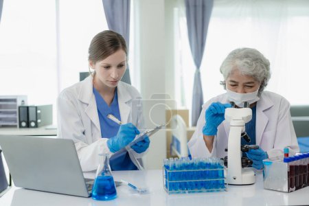 Photo for Beautiful young female scientist and two elderly women work in a laboratory with test tubes researching blue chemicals in the healthcare industry. - Royalty Free Image