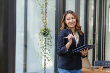 Téléchargez les photos : Femme d'affaires debout avec tablette travaillant à côté du mur de verre dans le bureau, concept de travail en ligne - en image libre de droit