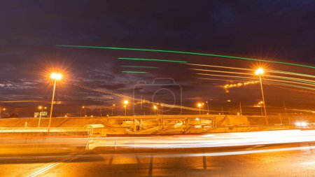 Téléchargez les photos : Mouvement temporel de la conduite rapide de nuit dans une grande ville de la fenêtre de la voiture en face de la route avec des lignes lumineuses des véhicules et des lampadaires. - en image libre de droit