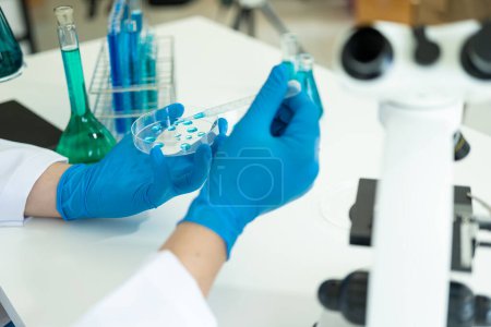 Foto de Doctor en máscara examinando molécula de ADN en laboratorio de química con científico examinando muestra líquida con microscopio en laboratorio de química Investigador trabajando con muestra - Imagen libre de derechos