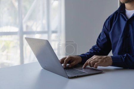 Foto de Joven hombre de negocios asiático que trabaja con el ordenador portátil, comprobación de gráficos, informes de presupuesto de la empresa, control de producción. Coste de inspección operativa más precio Imágenes de primer plano - Imagen libre de derechos