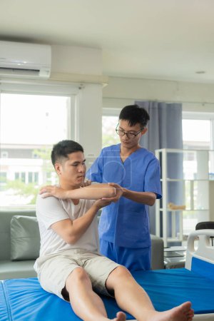 Foto de Médico examinando el brazo lesionado del paciente masculino, estiramiento y ejercicio Haciendo terapia del dolor, fisioterapeuta trabajando con el paciente en clínica cerrada - Imagen libre de derechos