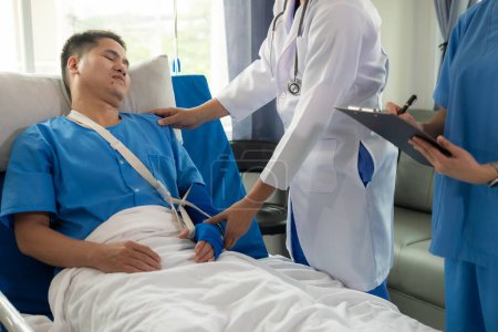 Foto de Paciente masculino en una cama de hospital con personal médico al lado de la cama que da aliento y consejos sobre el tratamiento. - Imagen libre de derechos