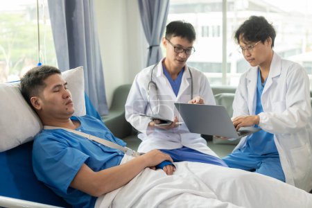 Foto de Paciente masculino en una cama de hospital con personal médico al lado de la cama que da aliento y consejos sobre el tratamiento. - Imagen libre de derechos