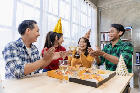 Photo for Group of happy Asian young people with friends celebrate clinking glasses during party, food, pizza, snacks with silverware Stemware glass and delicious food - Royalty Free Image