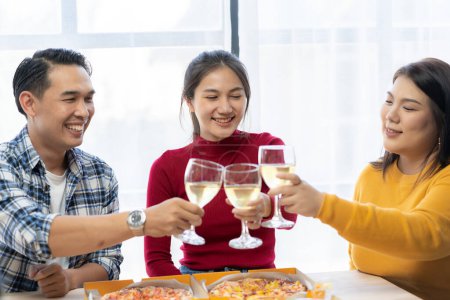 Téléchargez les photos : Groupe de jeunes Asiatiques heureux avec des amis célèbrent cliquetis lunettes pendant la fête, nourriture, pizza, collations avec argenterie Verrerie et nourriture délicieuse - en image libre de droit