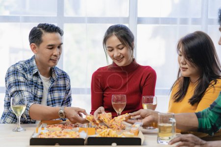 Foto de Grupo de jóvenes asiáticos felices con amigos celebran tintineo vasos durante la fiesta, comida, pizza, bocadillos con plata Stemware vidrio y deliciosa comida - Imagen libre de derechos