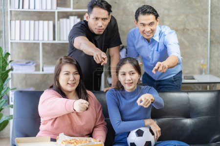 Foto de Jóvenes asiáticos sentados en el sofá viendo y animando el fútbol o el partido de fútbol en la televisión juntos en casa y celebrando la victoria. - Imagen libre de derechos