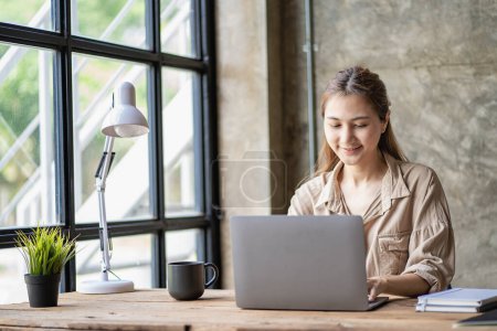 Photo for Asian student, young female Millennial woman preparing for a test or surfing the web with a laptop in a coffee shop, taking notes in an online notebook, webinar, learning foreign languages - Royalty Free Image
