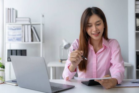 Téléchargez les photos : Jeune femme asiatique assise au bureau avec des données et du papier graphique à l'aide d'un ordinateur portable, l'analyse des comptes, des stratégies de planification sur l'amélioration des affaires au bureau. - en image libre de droit