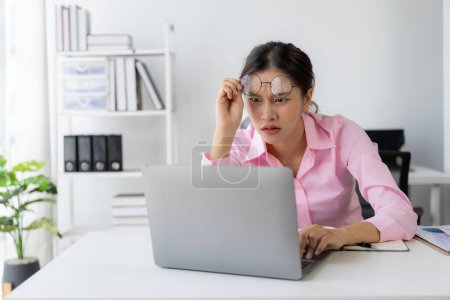 Photo for Young Asian woman sitting at desk with data and graph paper using laptop, analyzing accounts, planning strategies on business improvement in office. - Royalty Free Image