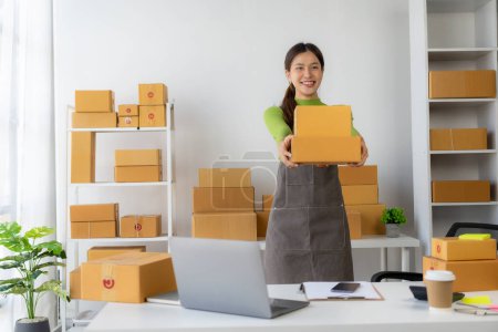 Photo for Start a small business SMEYoung Asian woman Business owner using smartphone or laptop receives and checks online orders to prepare boxes of products. Sale. - Royalty Free Image