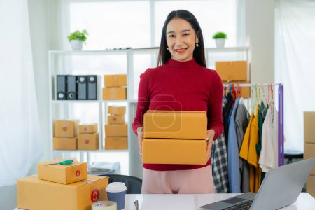Photo for Asian female entrepreneur SME business owner works with laptop, box and phone to shop online at home. Online Marketing SME Ecommerce Online Packaging Delivery - Royalty Free Image