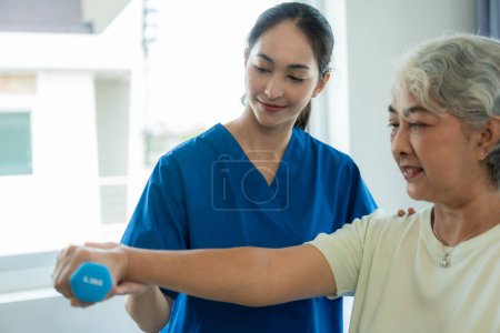 Foto de Una joven enfermera asiática en un asilo cuida de una mujer mayor. El médico que atiende proporciona servicios de fisioterapia para que los pacientes de edad avanzada hagan ejercicio para su salud. - Imagen libre de derechos